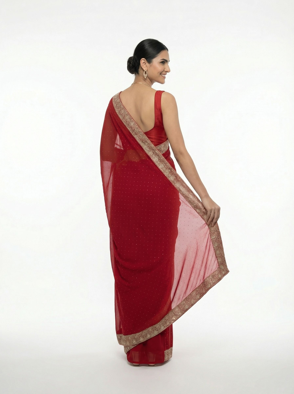 Woman in a red saree standing in an outdoor setting with decorative elements.