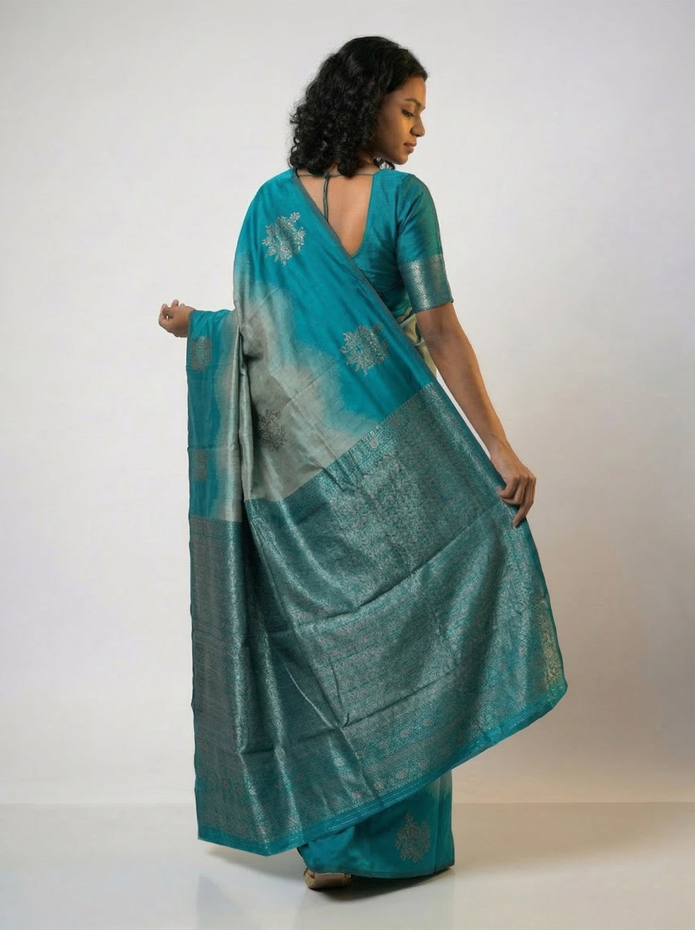 Woman wearing a teal saree with a subtle pattern on a pink background