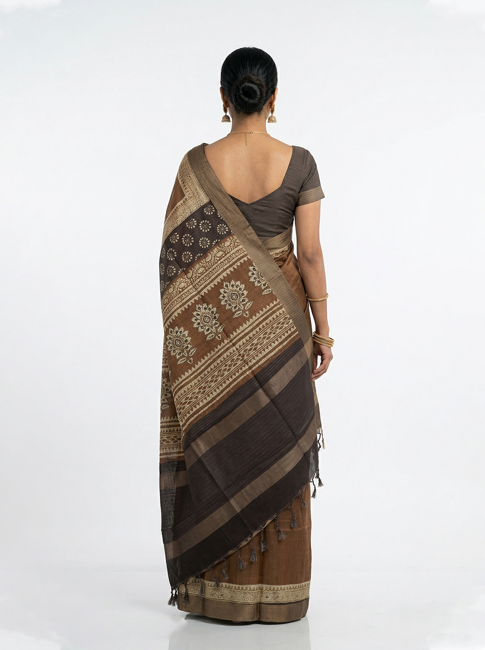 Woman in a brown saree standing in an ornate hallway