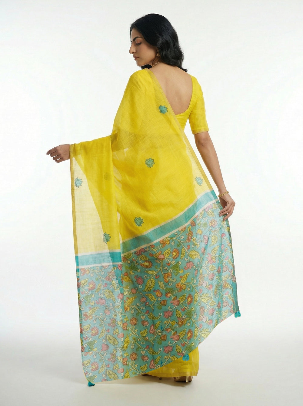 Woman in a yellow saree standing in a room with wooden furniture and decor.