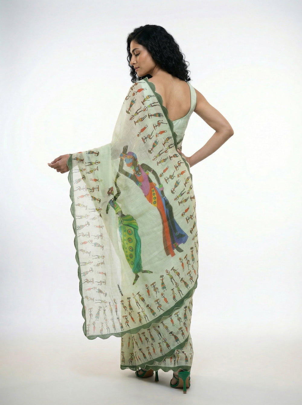 Woman in a light green saree standing in a room with a mirror and plants.