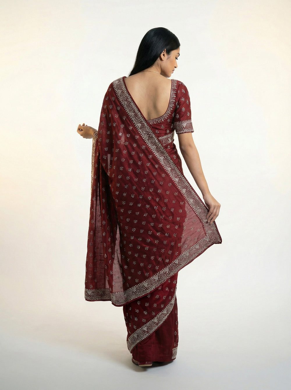 Woman in a maroon saree standing in a garden setting