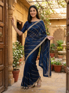Woman in a blue saree standing in a decorative outdoor setting with plants and architectural elements.