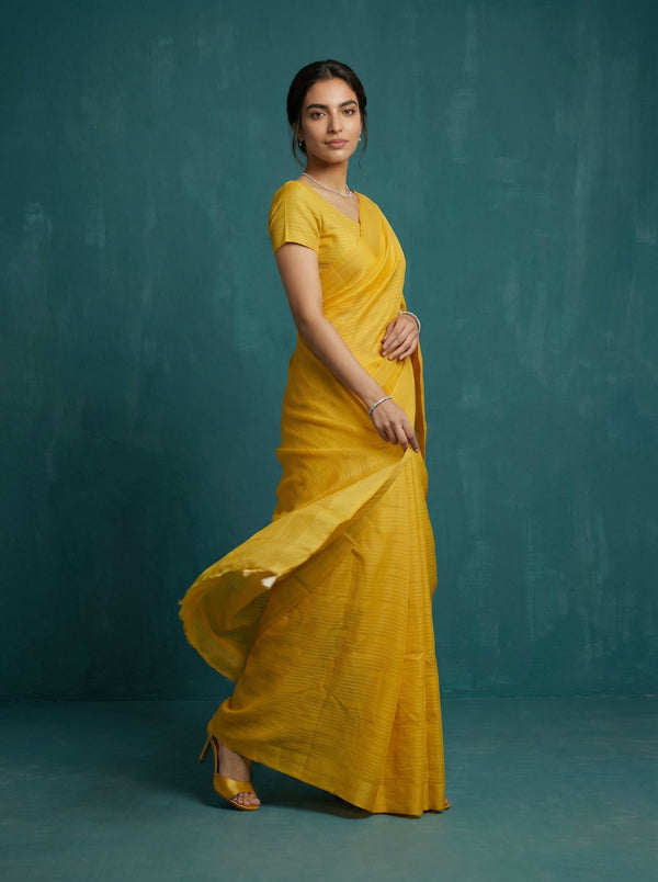 Woman wearing a yellow saree against a teal background