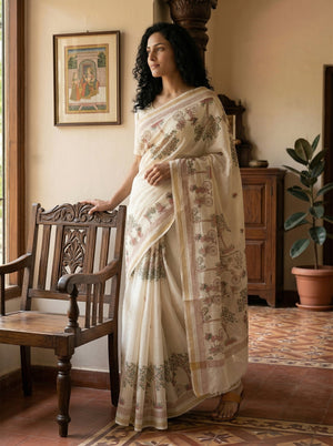 Woman in a traditional saree standing in a room with wooden furniture and decor.