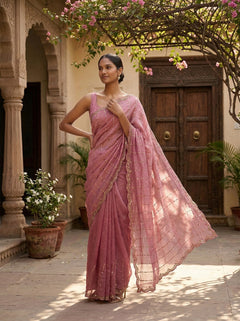 Woman in a pink saree standing in a courtyard with floral decorations.