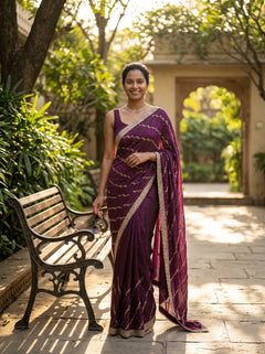 Woman in a purple saree standing outdoors with greenery and a bench in the background