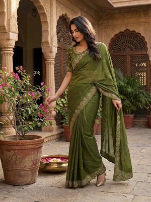 Woman in a green saree standing in an outdoor setting with plants and architectural elements.