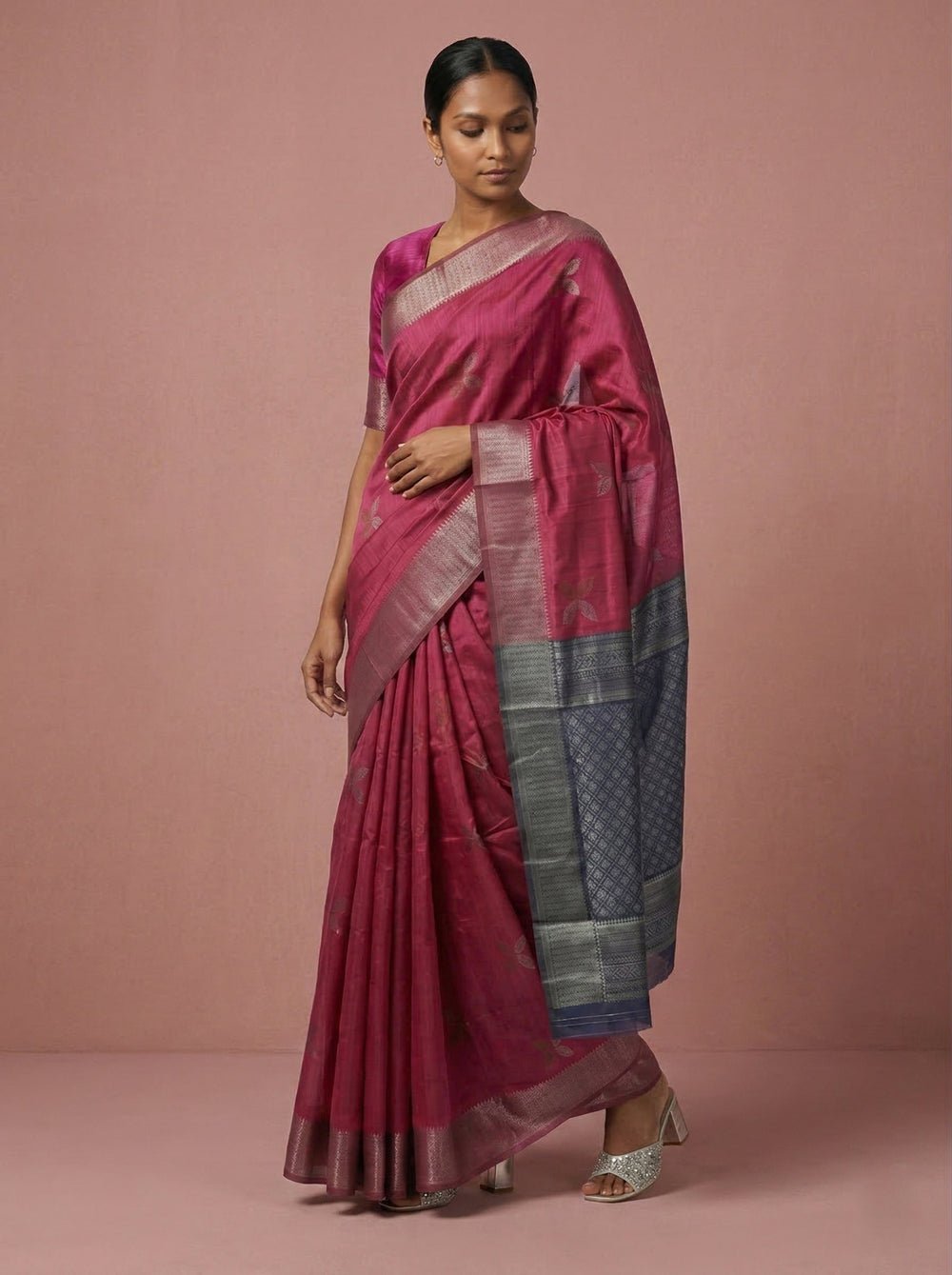 Woman wearing a pink saree with a patterned border against a pink background