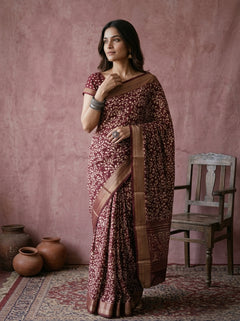 Woman in a patterned saree standing against a pink wall with rustic decor.