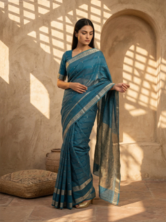 Woman in a blue saree standing in a sunlit room with architectural elements.
