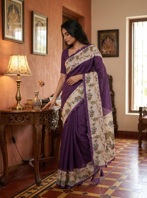 Woman in a purple saree standing in a room with decorative elements.