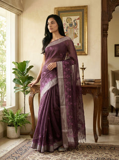 Woman in a purple saree standing in a room with decor elements.