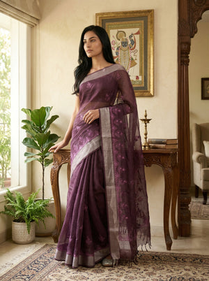 Woman in a purple saree standing in a room with decor elements.