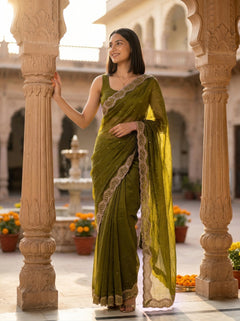 Woman in a green saree with gold border standing in an ornate architectural setting.