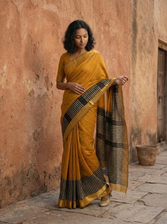 Woman in a mustard yellow saree standing against a textured wall.