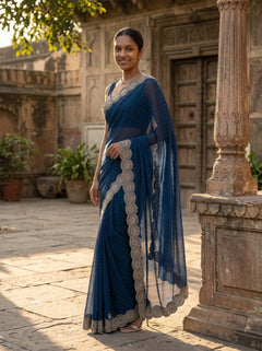 Woman in a blue saree standing in front of an old building with stone architecture.