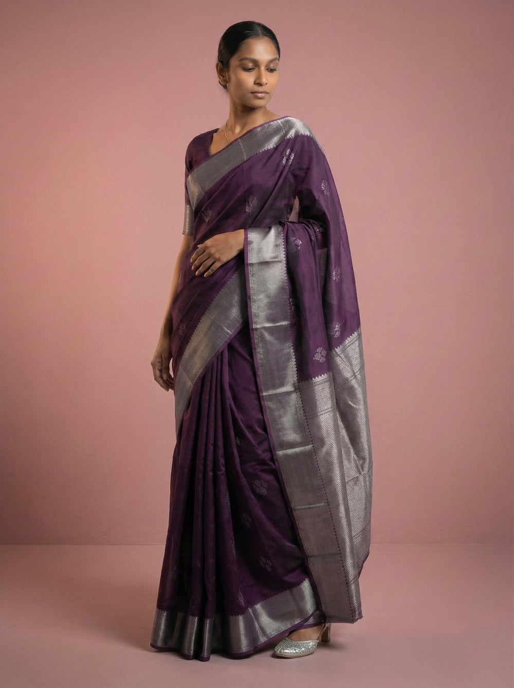 Woman wearing a purple saree with silver border against a pink background