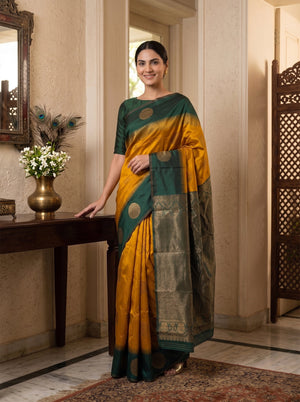 Woman in a green and yellow saree standing in a room with a decorative table and mirror.