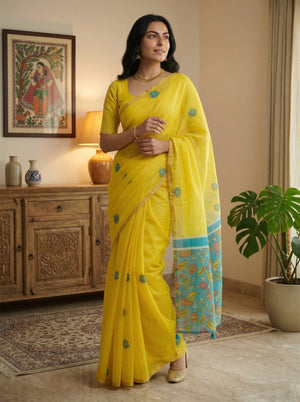 Woman in a yellow saree standing in a room with wooden furniture and decor.
