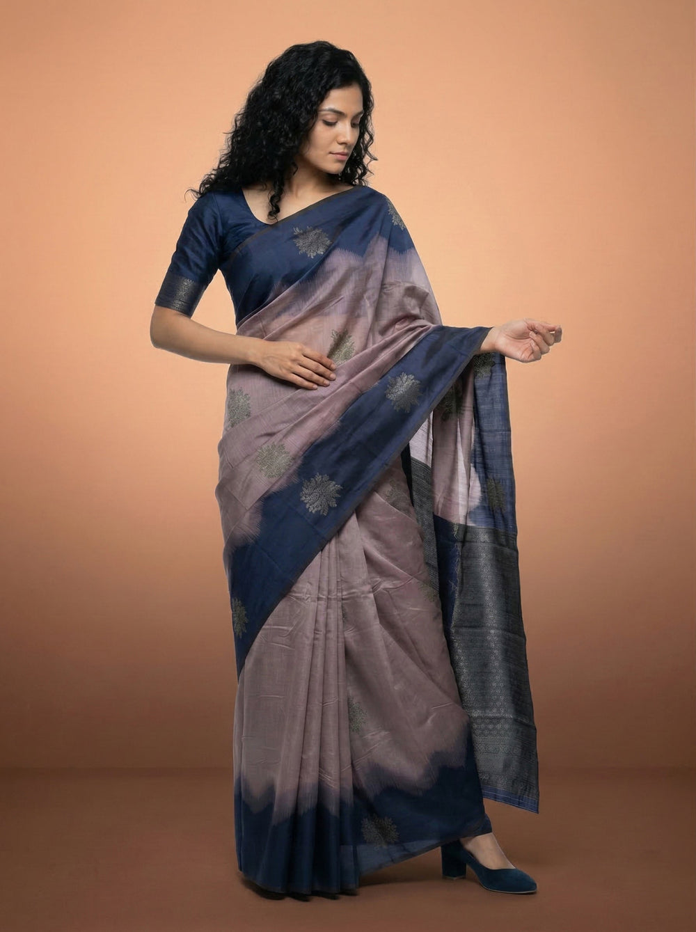 Woman wearing a blue and gray saree against a beige background