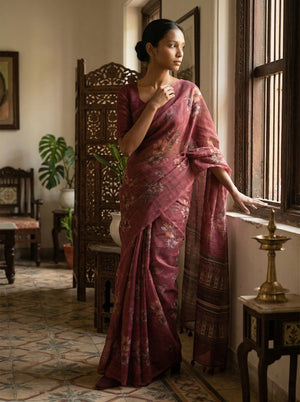 Woman in a traditional maroon saree standing by a window in a room with decorative elements.