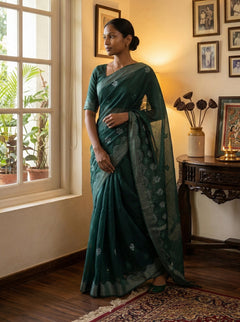 Woman in a green saree standing by a window in a room with decor elements.