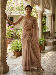 Woman in a traditional saree standing in an outdoor setting with plants and architectural elements.