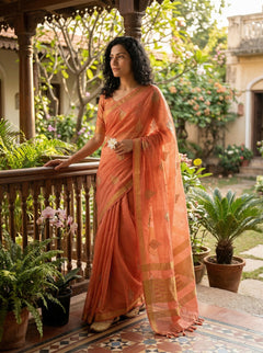 Woman in an orange saree standing on a balcony with plants and garden view