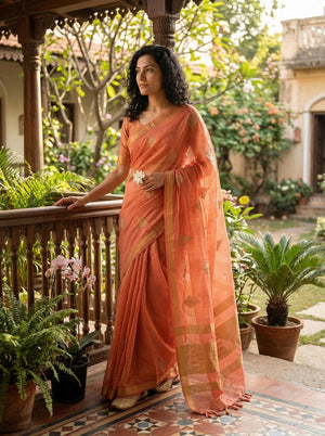 Woman in an orange saree standing on a balcony with plants and garden view