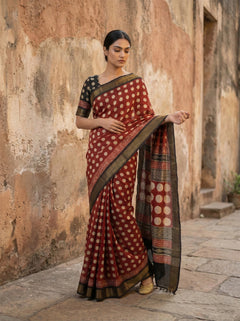 Woman wearing a traditional saree with a patterned design against an old stone wall.