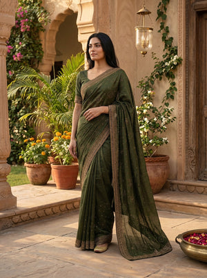 Woman in a green saree standing in an outdoor setting with plants and architectural elements.