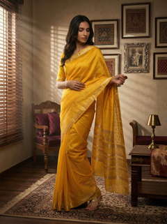 Woman in a yellow saree standing in a room with framed pictures on the wall.