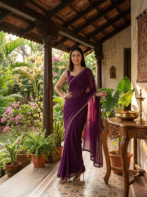 Woman in a purple saree standing in a garden setting with plants and a table.