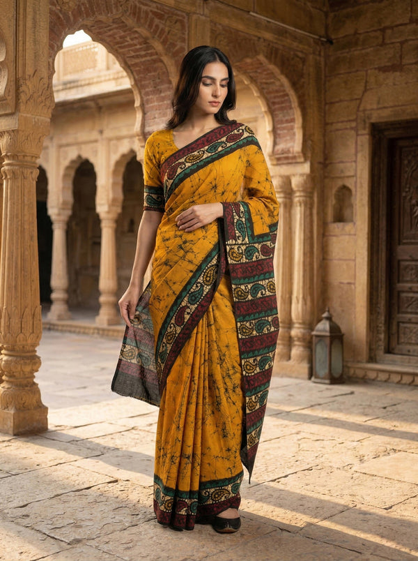 Woman in a yellow saree with a patterned border standing in an architectural setting.