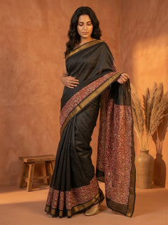 Woman wearing a black saree with a patterned border against an orange background