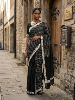 Woman in a black and white saree standing in front of a stone building with a door.