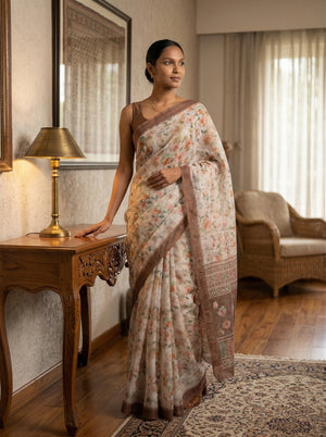 Woman in a floral saree standing in a room with a lamp and couch.