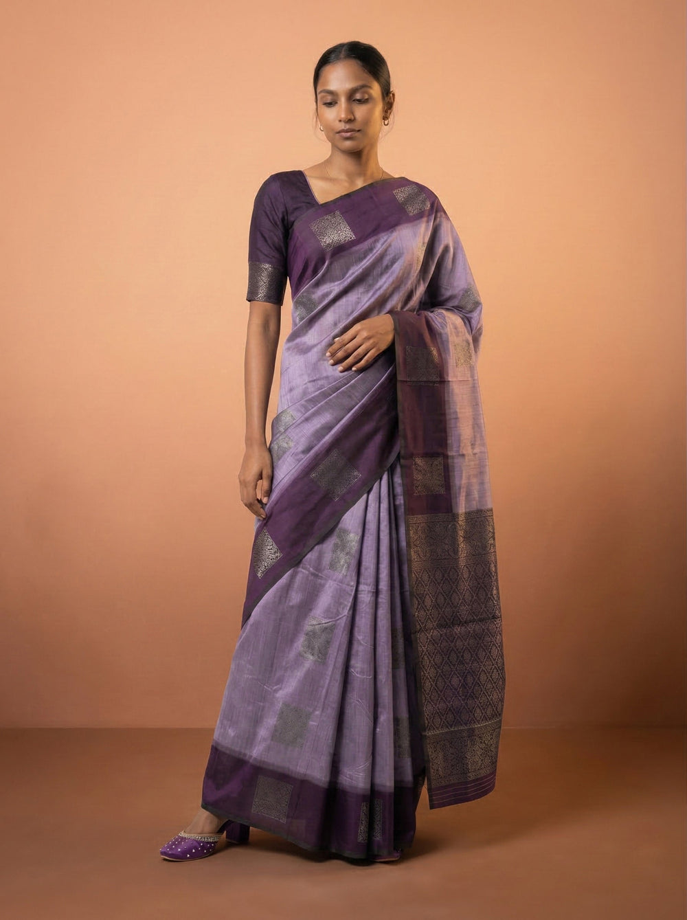 Woman wearing a purple saree with a subtle pattern on a peach background