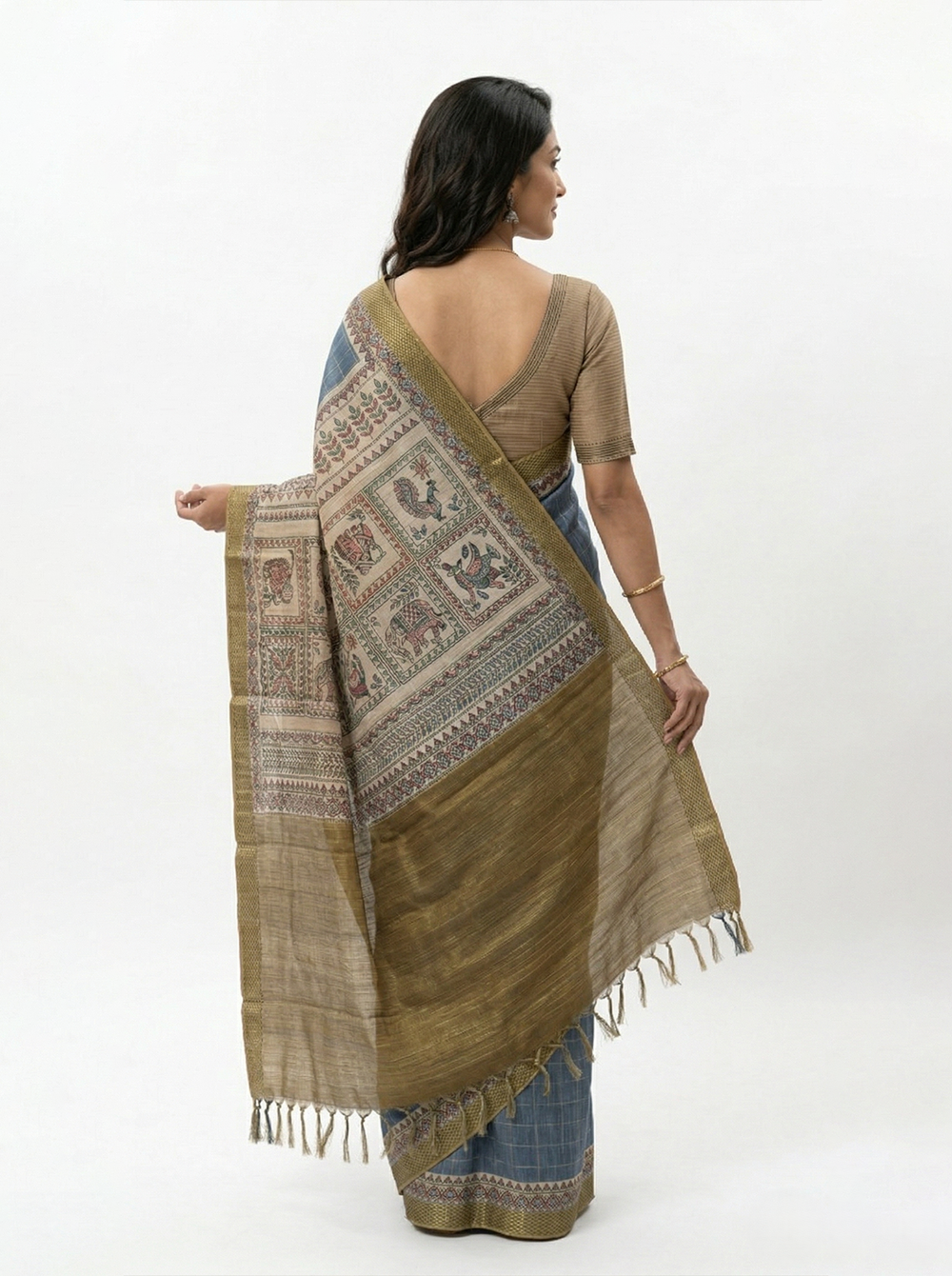 Woman in a blue saree with gold border standing on a road with greenery in the background
