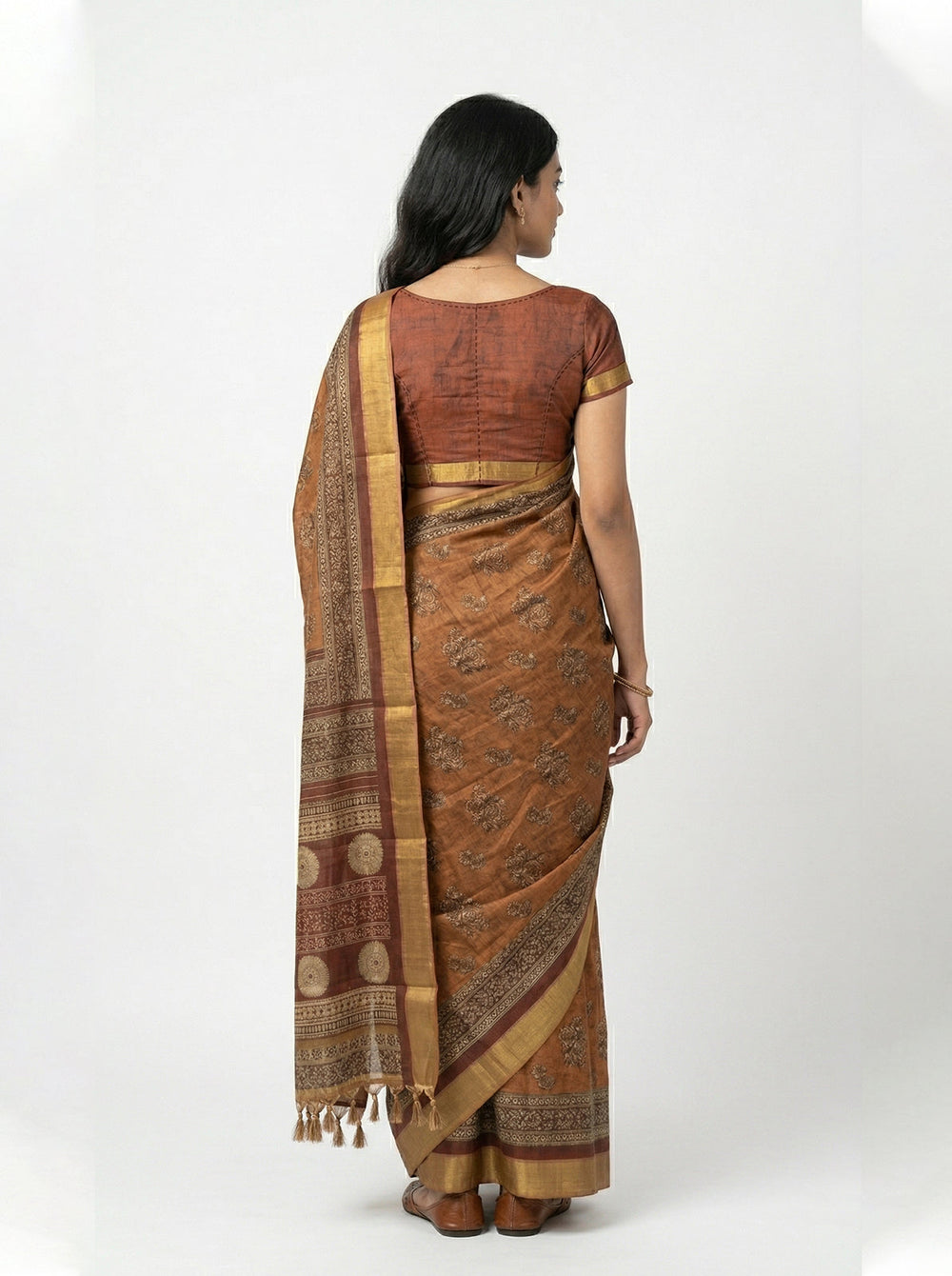 Woman in a traditional brown and gold saree standing on red flowers with a brown background