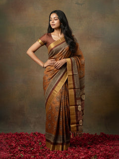 Woman in a traditional brown and gold saree standing on red flowers with a brown background