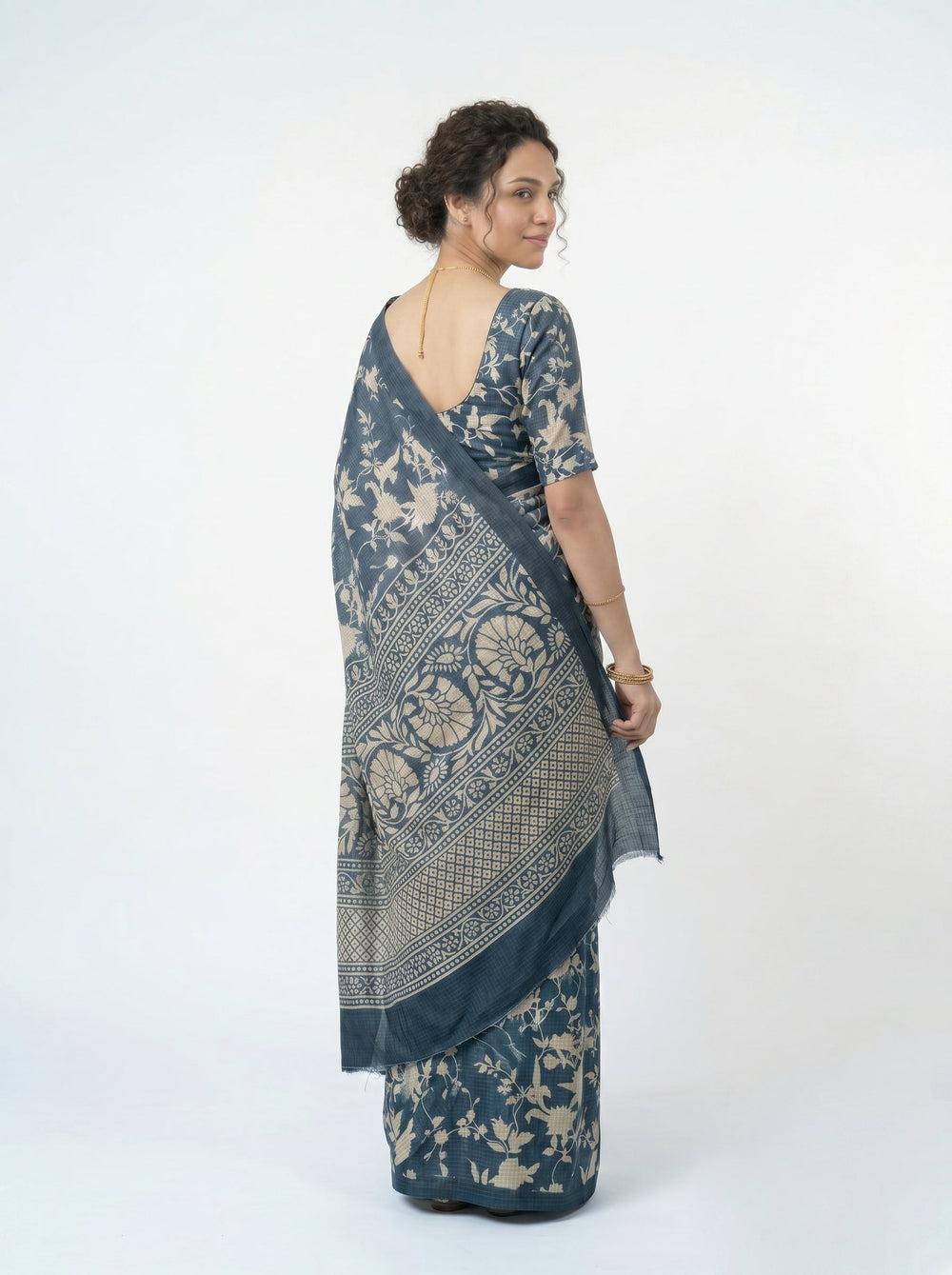 Woman wearing a blue saree with a floral pattern in a room with a window and decorative elements.