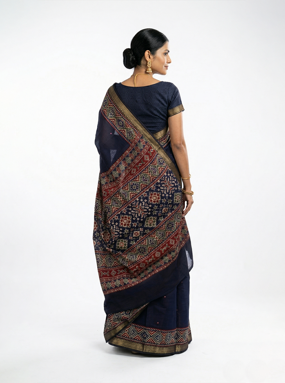 Woman in a traditional navy blue saree with a patterned border standing outdoors on a tree-lined path.