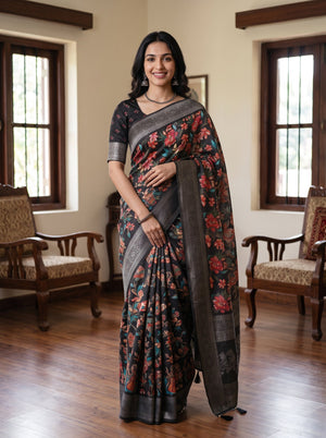 A woman modeling a dark gray and black floral saree with red and orange floral motifs, paired with a black printed blouse, standing in a traditional room with wooden floors and windows.