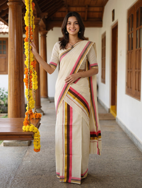 A woman wearing a cream-colored cotton saree with pink, yellow, and green striped borders stands on a traditional porch with wooden pillars and hanging marigold garlands.