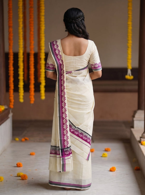 A woman viewed from behind wearing a cream-colored cotton saree with purple and black border patterns, standing in a corridor decorated with hanging marigold garlands.