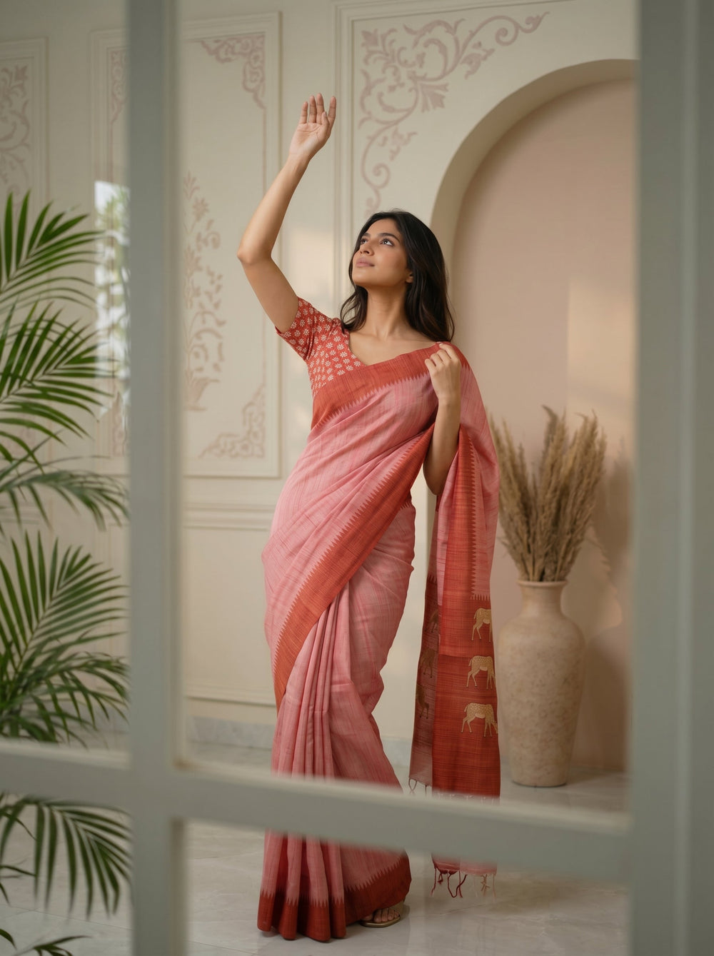 Woman in a pink saree standing in a room with decorative elements.