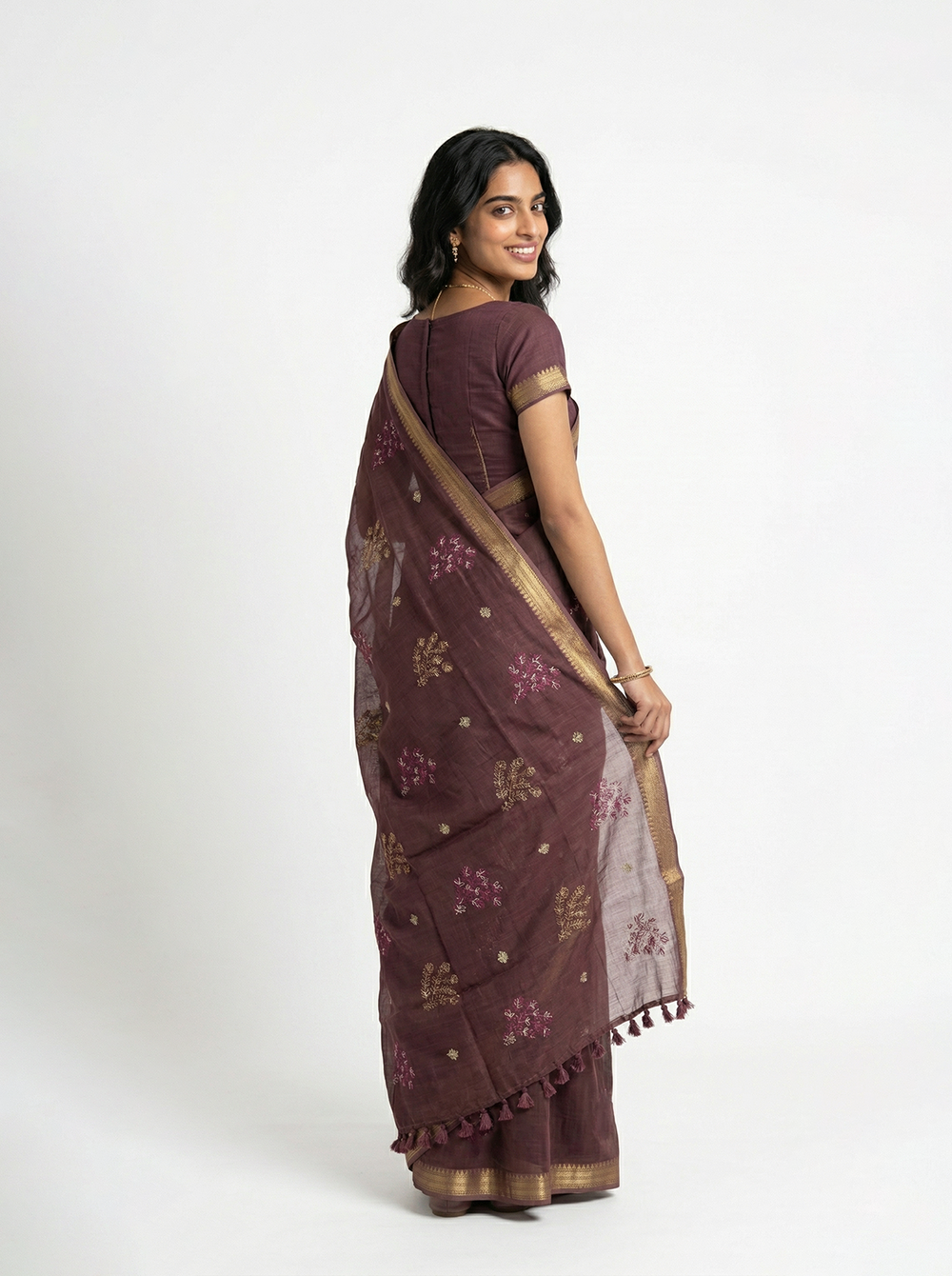 Woman in a brown saree standing by a window in a room with a couch and plant.