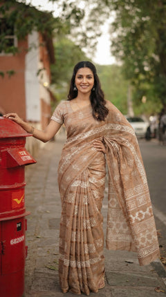 Woman in a beige saree standing next to a red mailbox on a street.